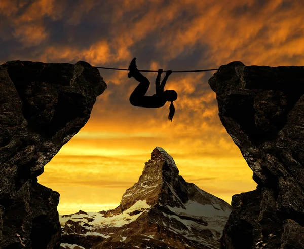Silhouette girl climbs on a rope over an abyss. — Stock Photo, Image