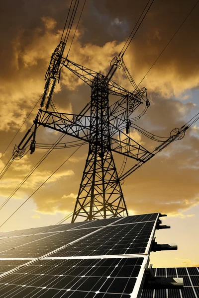 Zonnepanelen met hoogspanningsmast bij zonsondergang. — Stockfoto