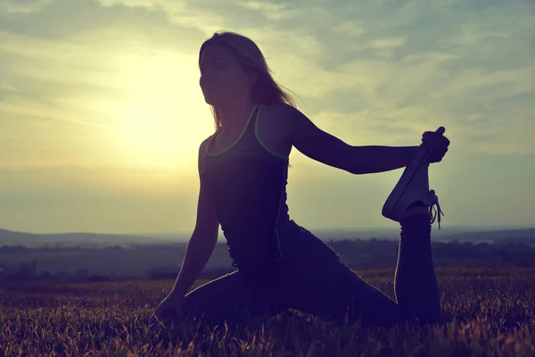Silhouette of young woman stretching on a meadow — Stock Photo, Image