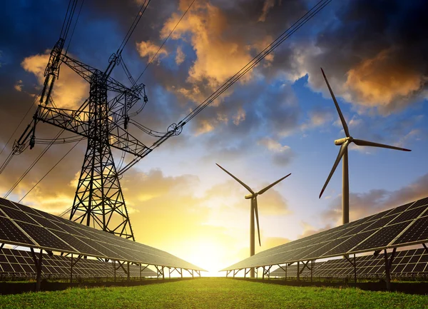 Zonnepanelen met windturbines en hoogspanningsmast bij zonsondergang. — Stockfoto