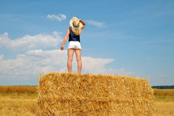 Woman with hat standing on a bale of straw — Stock Photo, Image
