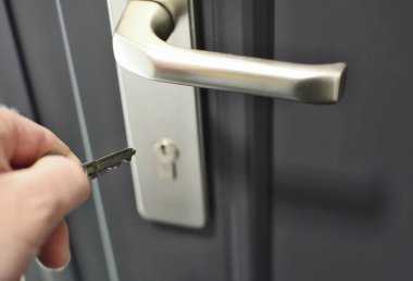Kapının kilidine anahtar sokmak için anahtar tutan bir el. Güvenlik kilidini açmak.