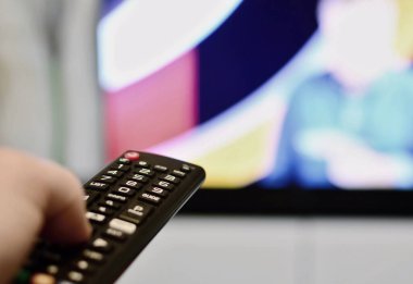 Televizyon kanallarını değiştiren uzaktan kumandayı tutan bir eli kapat. Uzaktan kumandayla TV değiştiriliyor. TV uzaktan kumandası kullanılıyor.