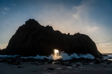 Pfeiffer Sahili, Kaliforniya 'daki anahtar deliği kemerinin geniş açılı görüntüsü, batan güneşi merkez delikten gözetliyor. Kaliforniya 'da bir kış akşamında gün batımı.