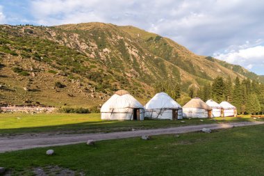 Kırgızistan 'ın yüksek dağlarındaki geleneksel Yurt kampını içeren bir manzara fotoğrafı..