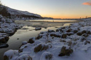 Landscape shot highlighting the rugged mountains and snow-covered beaches of arctic norway during a brief golden hour during the long winters.