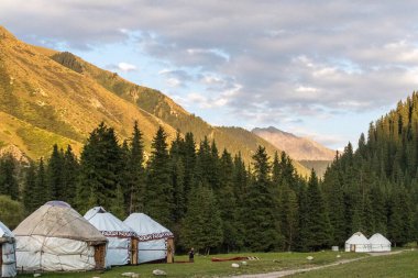Jeti-Oğuz Bölgesi, Kırgızistan - 10 Ağustos 2025. Kırgızistan dağlarında geleneksel bir yurt kampını akşam erken saatlerde ve gün batımından hemen önce gösteren açık hava sahnesi..