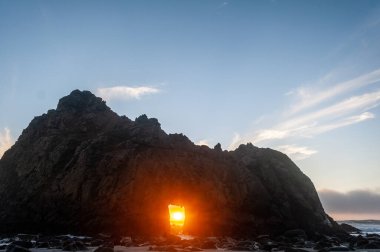 Pfeiffer Sahili, Kaliforniya 'daki anahtar deliği kemerinin geniş açılı görüntüsü, batan güneşi merkez delikten gözetliyor. Kaliforniya 'da bir kış akşamında gün batımı.