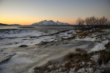 Landscape shot highlighting the rugged mountains and snow-covered beaches of arctic norway during a brief golden hour during the long winters.