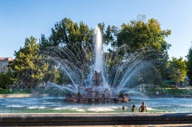 Taşkent, Özbekistan - 5 Ağustos 2025. Serinlemek isteyen insanların yakın çekimi bir çeşmedeki kavurucu sıcaklığı oluşturur. Bu çeşme Taşkent şehir merkezinde yer almaktadır..