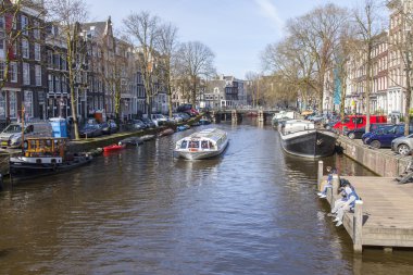 Amsterdam, Hollanda 1 Nisan 2016 üzerinde. Bahar sabahı tipik kent görünümünde. Kanal ve XVII-XVIII inşaat bentleri üzerinde binalar. Yürüyen gemi kanalda yüzen