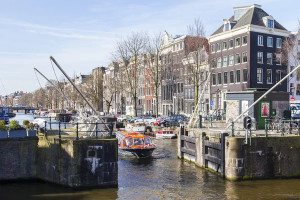 AMSTERDAM, NETHERLANDS on April 1, 2016. Типичный вид на город весной утром. Канал и здания XVII-XVIII вв. постройки на набережных. Ходячий корабль плавает по каналу — стоковое фото