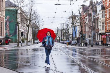 Amsterdam, Hollanda, 27 Mart 2016 tarihinde. Bahar sabahı tipik şehir manzarası. Kırmızı şemsiyeli kadın yağmurda sokağa iniyor.
