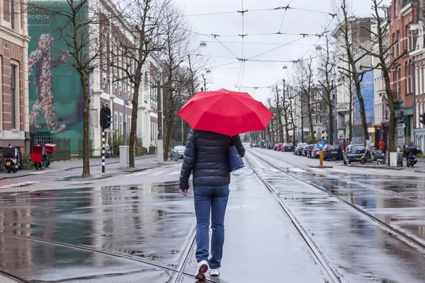 AMSTERDAM, PAYS-BAS, le 27 mars 2016. Vue urbaine typique le matin du printemps. La femme avec un parapluie rouge descend la rue sous la pluie — Photo