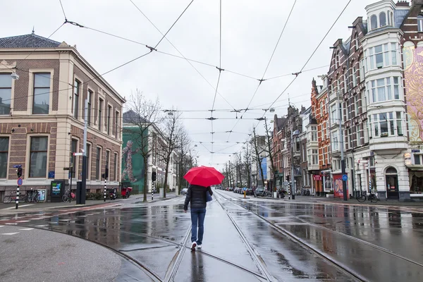 荷兰阿姆斯特丹，2016 年 3 月 27 日。春天早晨典型的城市景观。那个带着红伞的女人在雨中走在街上 — 图库照片