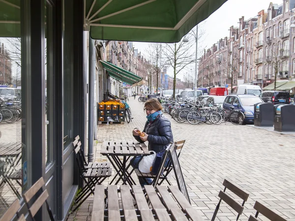 Amsterdam, Holandia, 27 marca 2016. Typowy widok miejski w wiosenny poranek. Kobieta siedzi przy małym stole ulicznej kawiarni — Zdjęcie stockowe