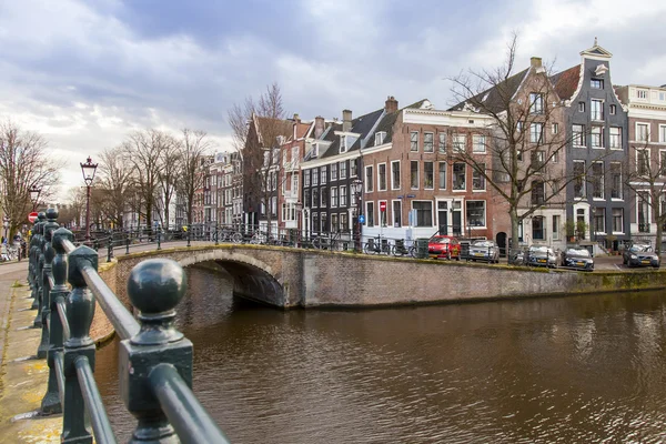 AMSTERDAM, NETHERLANDS on MARCH 27, 2016. Typical urban view in the spring evening. The bridge through the canal and buildings of the XVII-XVIII construction on embankments — Stock Photo, Image