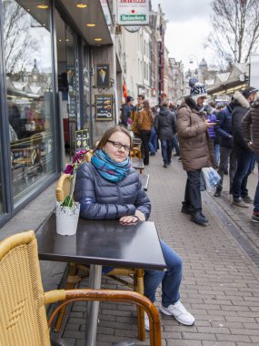 Amsterdam, Hollanda üzerinde 27 Mart 2016. Bahar sabahı tipik kent görünümünde. Açık havada yaz kafe küçük tablolar. Kadın bir dinlenme bir tablo vardır.