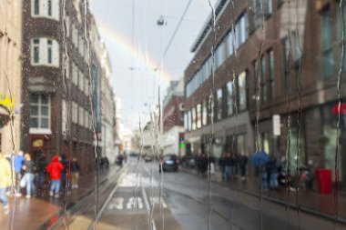 Amsterdam, Hollanda üzerinde 27 Mart 2016. Bahar öğleden sonra yağmur tramvay ıslak bir pencereden boyunca şehirde bir görüntü. Uzaktan gökyüzünde bir gökkuşağı