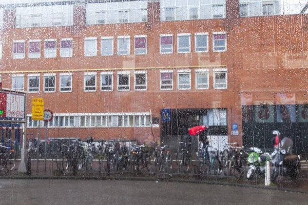 Amsterdam, Niederlande am 27. März 2016. Blick auf die Stadt am Frühlingnachmittag während eines Regens durch ein nasses Fenster der Straßenbahn. ein Regenbogen am Himmel in der Ferne — Stockfoto