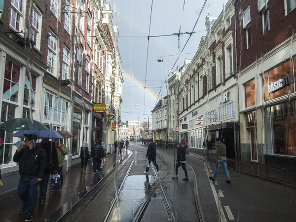 AMSTERDAM, PAÍSES BAJOS el 27 de marzo de 2016. Una vista de la ciudad en la tarde de primavera durante una lluvia a través de una ventana húmeda del tranvía. Un arco iris en el cielo en la distancia —  Fotos de Stock