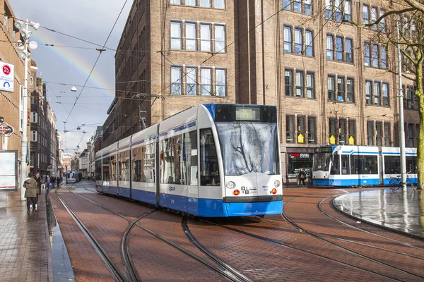 Amsterdam, Nizozemsko na 27 březen 2016. Typický městský pohled jarního odpoledne. Tramvaj se pohybuje dolů na ulici. Duha na obloze v dálce — Stock fotografie