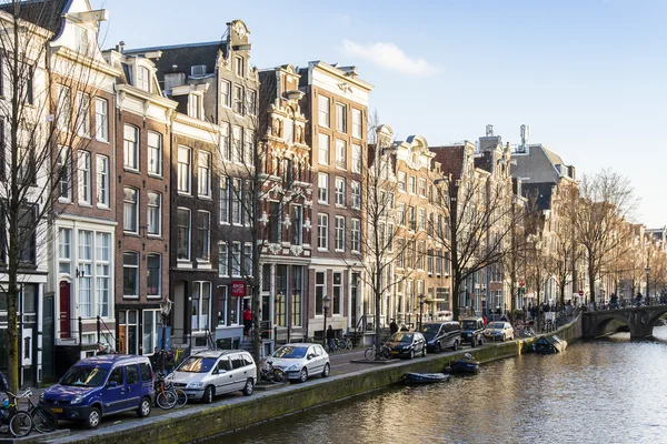 Amsterdam, Nizozemsko na 28 březnu 2016. Typický městský pohled jarního odpoledne. Kanál a budovy stavby Xvii a Xviii na náspy. Chodící loď pluje na kanálu — Stock fotografie