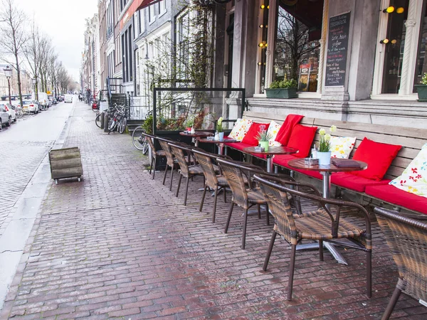 AMSTERDAM, PAÍSES BAJOS 28 DE MARZO DE 2016. Típica vista urbana en la noche de primavera. Pequeñas mesas de café de verano en la acera . — Foto de Stock