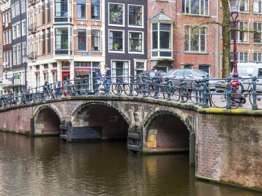 Amsterdam, Hollanda üzerinde 29 Mart 2016. Bahar öğleden sonra tipik kent görünümünde. Bisiklet bdge yolu ile belgili tanımlık kanal üzerinde park edilmiş