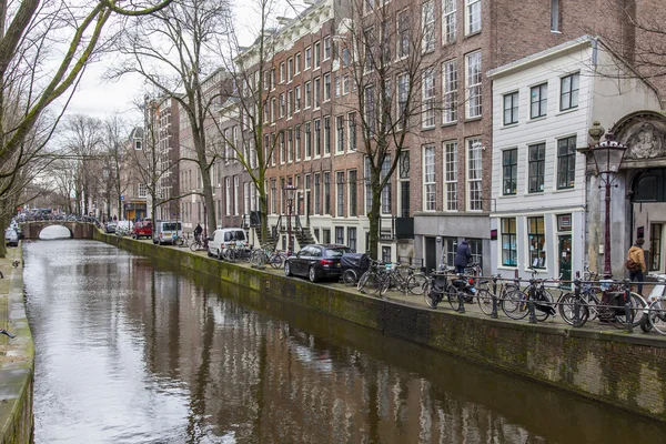 AMSTERDAM, NETHERLANDS on MARCH 27, 2016. Typical urban view in the spring evening. The bridge through the canal and buildings of the XVII-XVIII construction on embankments — Stock Photo, Image