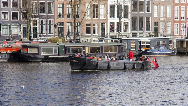 AMSTERDAM, NETHERLANDS on MARCH 27, 2016. Typical urban view. The walking ship with people and bar is onboard floats down by river Amstel — Stock Photo, Image