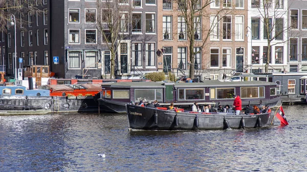 AMSTERDAM, PAÍSES BAJOS el 27 de marzo de 2016. Típica vista urbana. El barco a pie con gente y bar está a bordo flota por el río Amstel — Foto de Stock