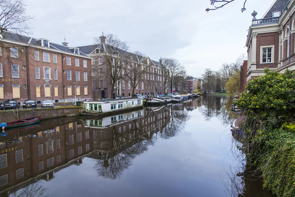 AMSTERDAM, PAÍSES BAJOS 31 DE MARZO DE 2016. Vista típica urbana en primavera. Edificios de la construcción XVII-XVIII sobre terraplenes. Casas flotantes cerca de banco — Foto de Stock