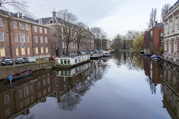 AMSTERDAM, PAÍSES BAJOS 31 DE MARZO DE 2016. Vista típica urbana en primavera. El canal y los edificios de la construcción XVII-XVIII sobre terraplenes. Casas flotantes cerca de banco —  Fotos de Stock
