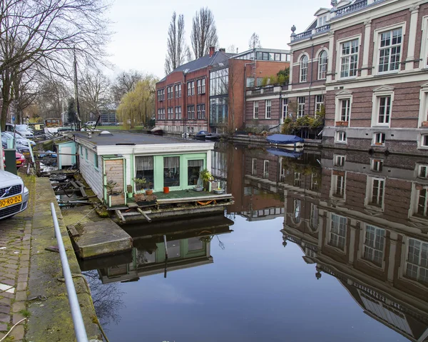 AMSTERDAM, PAÍSES BAJOS 31 DE MARZO DE 2016. Vista típica urbana en primavera. El canal y los edificios de la construcción XVII-XVIII sobre terraplenes. Casas flotantes cerca de banco —  Fotos de Stock