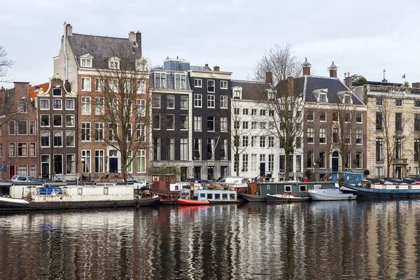 AMSTERDAM, PAYS-BAS, le 31 mars 2016. Vue urbaine typique au printemps. Le canal et les bâtiments de la construction XVII-XVIII sur les remblais. Péniches près de la banque — Photo
