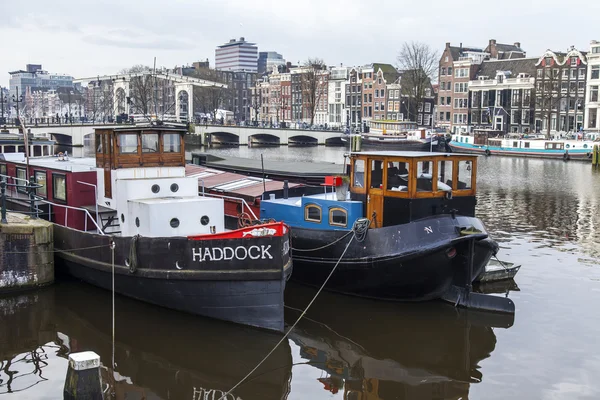 AMSTERDAM, PAÍSES BAJOS 31 DE MARZO DE 2016. Vista típica urbana en primavera. El canal y los edificios de la construcción XVII-XVIII sobre terraplenes. Casas flotantes cerca de banco — Foto de Stock