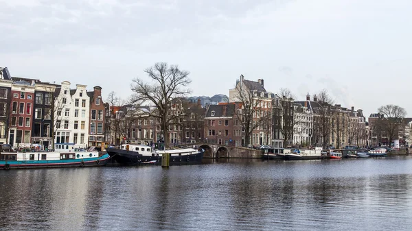 AMSTERDAM, PAÍSES BAJOS 31 DE MARZO DE 2016. Vista típica urbana en primavera. El río Amstel y los edificios de la construcción XVII-XVIII sobre terraplenes. Casas flotantes cerca de banco — Foto de Stock