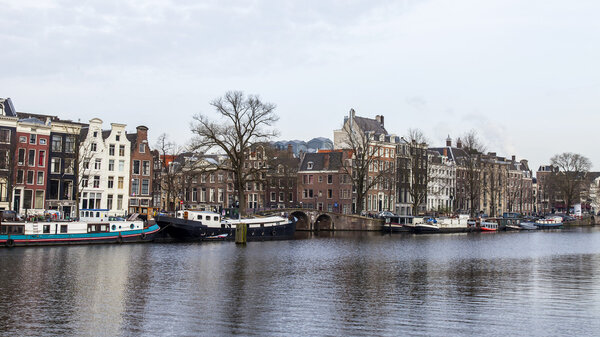 AMSTERDAM, NETHERLANDS on MARCH 31, 2016. Typical urban view in the spring. The river Amstel and buildings of the XVII-XVIII construction on embankments. Houseboats near bank
