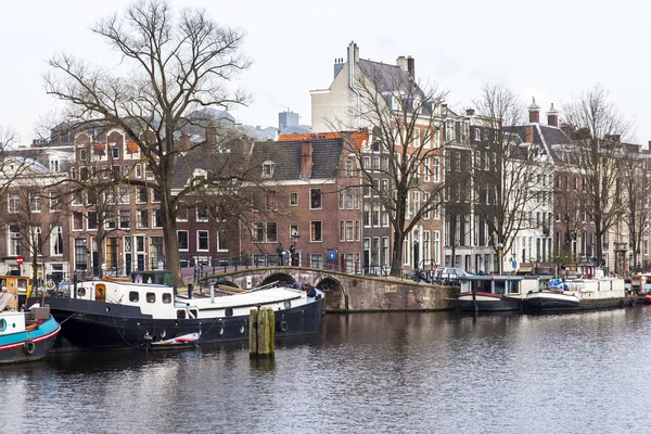 Amsterdam, Nizozemsko na 31 březnu 2016. Typický městský pohled na jaře. Řeka Amstel a budovy stavby Xvii a Xviii na náspy. Hausbóty u banky — Stock fotografie