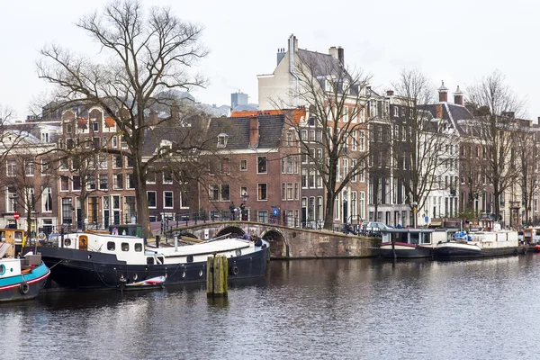 AMSTERDAM, PAÍSES BAJOS 31 DE MARZO DE 2016. Vista típica urbana en primavera. El río Amstel y los edificios de la construcción XVII-XVIII sobre terraplenes. Casas flotantes cerca de banco —  Fotos de Stock