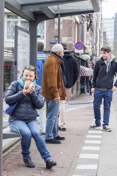 Amsterdam, Nederland op 31 maart 2016. Typisch stedelijke weergave in de lentemorgen. Mensen wachten op de tram bij een halte. De vrouw eet traditionele Nederlandse haring sandwich — Stockfoto