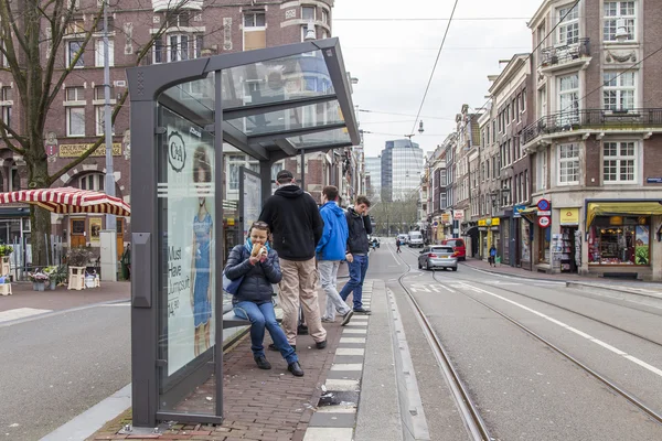 Amsterdam, Nizozemsko na 31 březnu 2016. Typický městský pohled v jarní ráno. Lidé čekat na tramvaj na zastávce. Žena jí tradiční holandské sledě sendvič — Stock fotografie
