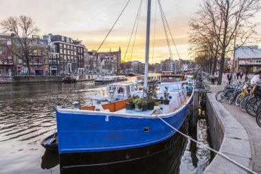 AMSTERDAM, NETHERLANDS on MARCH 31, 2016. A typical urban view during sunset. The Amstel river and buildings of the XVII-XVIII construction on embankments. Vessels moored near bank clipart