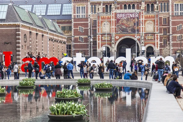 Amsterdam, Nederländerna på den 31 mars, 2016. Museumplein. Rijksmuseum. Turister har en god tid nära inskriptionen jag Amsterdam. Fontänen av blomkrukor med tulpaner — Stockfoto