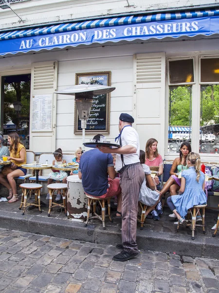 PARIS, FRANÇA, em 8 de julho de 2016. Montmartre, as pessoas comem e descansam atrás de mesas de café na calçada. O garçom em roupas vintage serve os visitantes — Fotografia de Stock