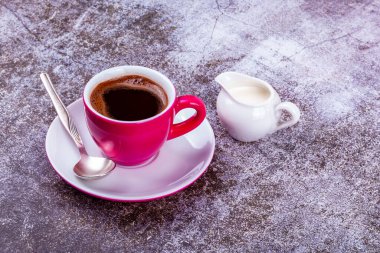 Pembe porselen bardakta espresso kahve ve porsiyonlu sürahide krema.