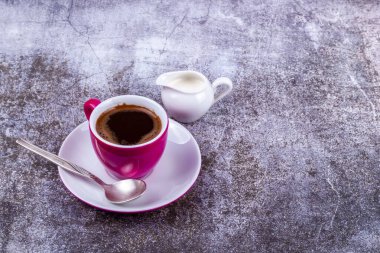Pembe porselen bardakta espresso kahve ve porsiyonlu sürahide krema.