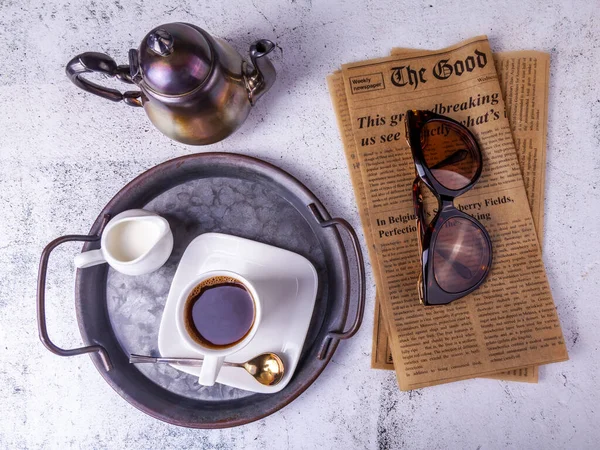 Vintage newspaper, pink porcelain coffee cup and glasses on a table in a cafe