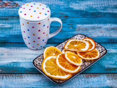 Dikdörtgen bir tabakta kurumuş portakal dilimleri ve onlardan içmek için bir bardak.